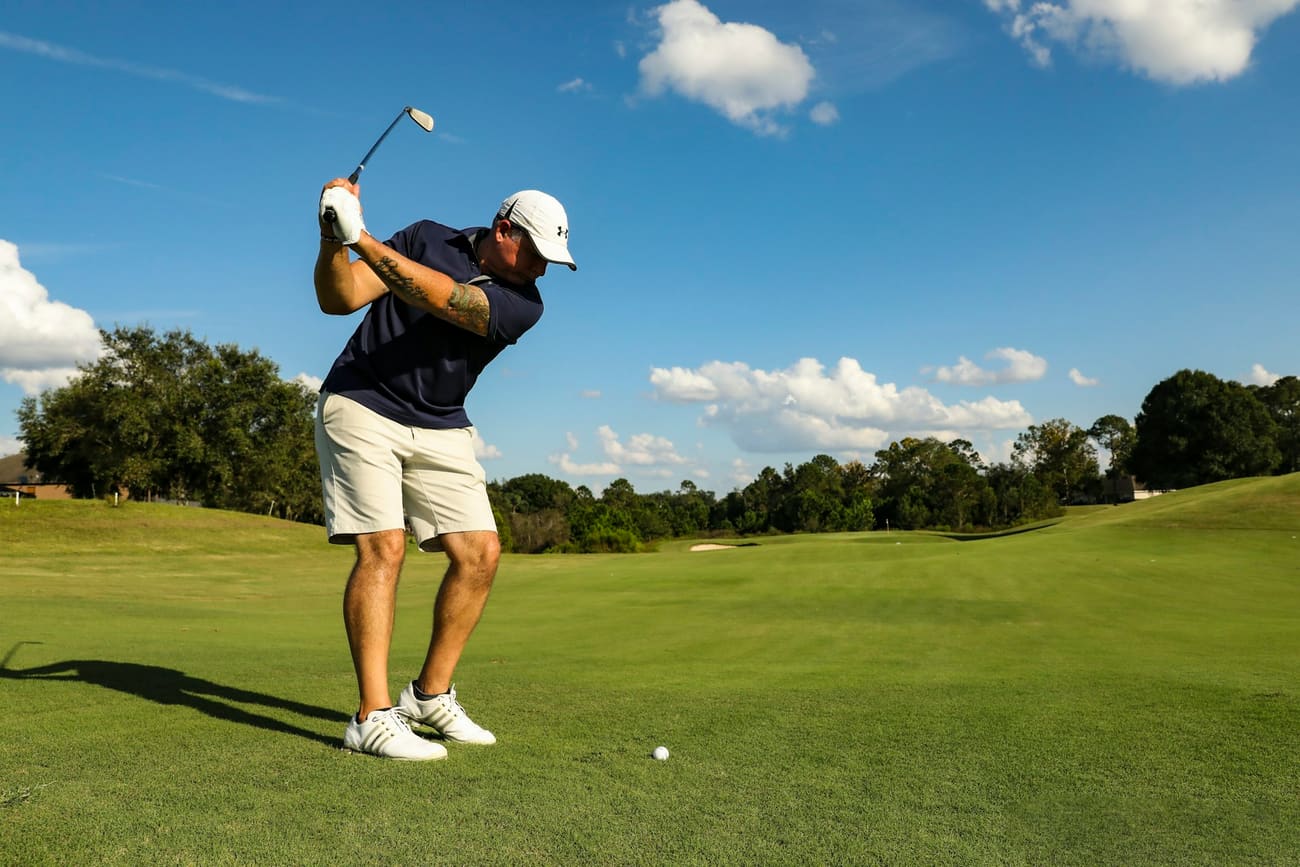A golfer at the top of the backswing on a sunlit fairway